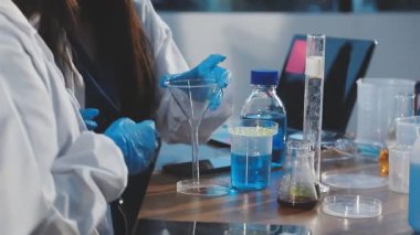 Koruyucu eldivenli ve ceketli bilim adamı laboratuarda test tüpleri yapıyor..