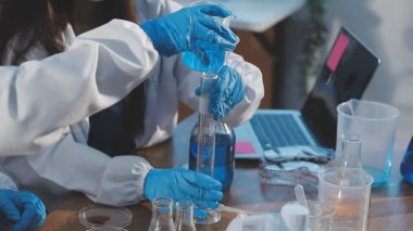 Laboratuvarda bir matara ve kimyasal bir deneyle çalışan koruyucu eldivenler giyen bilim adamı.