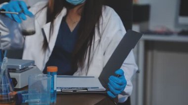 Laboratuvarda çalışan üniformalı genç bir kadın. Elinde bir mikroskop ve elinde bir matara var.