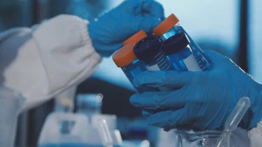 Koruyucu maskeli bilim adamı elinde bir deney tüpü tutuyor.