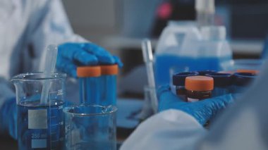 Yakın plan - koruyucu kıyafetli laboratuvar asistanının elinde pipetli test tüpleri.