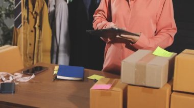 Takım elbiseli bayan girişimci evde paket kutularıyla çalışırken akıllı telefon kullanıyor.