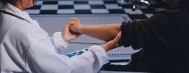 Ortopedi doktoru klinikte bileği ağrıyan bir hastayı muayene ediyor. Fizyoterapist bilek kemiğine bastırarak hastanın bileğini kontrol eder..