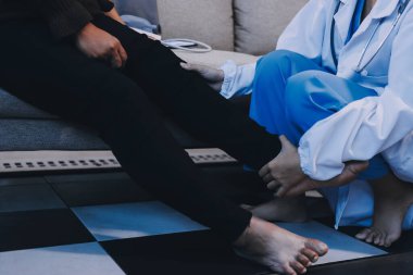 Genç doktor kıdemli hastanın bacağını muayene ediyor.