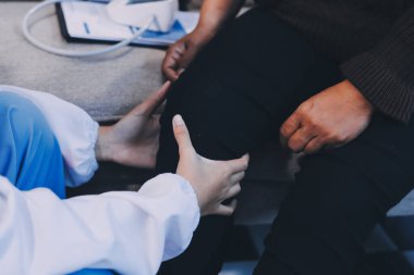 Genç doktor kıdemli hastanın bacağını muayene ediyor.