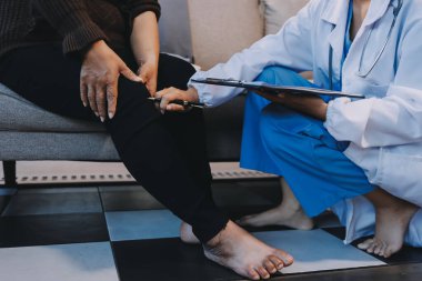 Genç doktor kıdemli hastanın bacağını muayene ediyor.