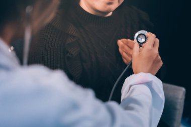 Ev bakımı hemşiresi ve yaşlılar kardiyoloji sağlık hizmetleri. Genç İspanyol kadın doktor hemşirenin yakın çekimleri sırasında steteskop kullanarak olgun beyaz hasta kalp atışlarını kontrol et.