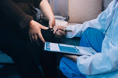 Genç doktor kıdemli hastanın bacağını muayene ediyor.