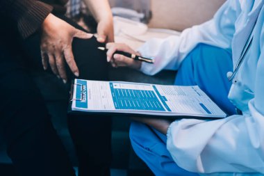 Genç doktor kıdemli hastanın bacağını muayene ediyor.