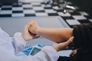 Ortopedi doktoru klinikte bileği ağrıyan bir hastayı muayene ediyor. Fizyoterapist bilek kemiğine bastırarak hastanın bileğini kontrol eder..