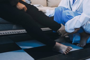 Genç doktor kıdemli hastanın bacağını muayene ediyor.