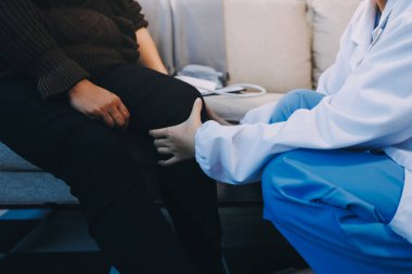 Genç doktor kıdemli hastanın bacağını muayene ediyor.