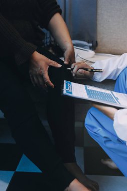 Genç doktor kıdemli hastanın bacağını muayene ediyor.