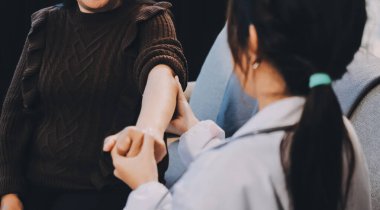 Ortopedi doktoru klinikte bileği ağrıyan bir hastayı muayene ediyor. Fizyoterapist bilek kemiğine bastırarak hastanın bileğini kontrol eder..