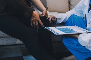 Genç doktor kıdemli hastanın bacağını muayene ediyor.