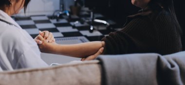 Ortopedi doktoru klinikte bileği ağrıyan bir hastayı muayene ediyor. Fizyoterapist bilek kemiğine bastırarak hastanın bileğini kontrol eder..