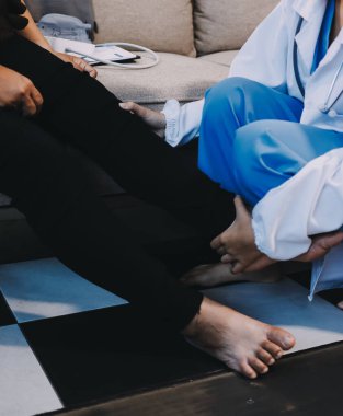 Genç doktor kıdemli hastanın bacağını muayene ediyor.