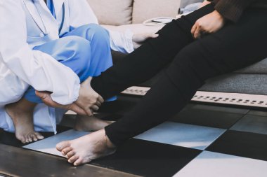 Genç doktor kıdemli hastanın bacağını muayene ediyor.