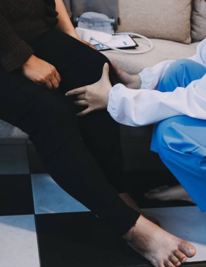 Genç doktor kıdemli hastanın bacağını muayene ediyor.