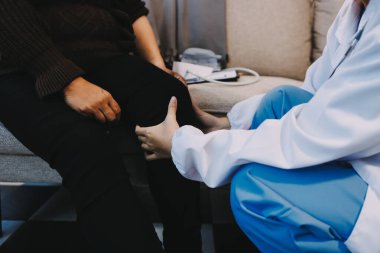 Genç doktor kıdemli hastanın bacağını muayene ediyor.