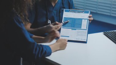 Ofiste bilgisayar üzerinde çalışırken elinde pano tutan mavi ceketli genç bayan doktor..