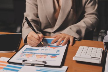 Group of confident business people point to graphs and charts to analyze market data, balance sheet, account, net profit to plan new sales strategies to increase production capacity.