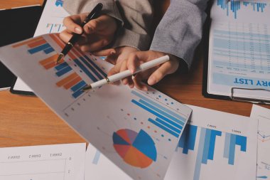 Group of confident business people point to graphs and charts to analyze market data, balance sheet, account, net profit to plan new sales strategies to increase production capacity.