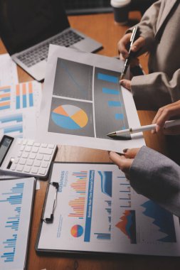 Group of confident business people point to graphs and charts to analyze market data, balance sheet, account, net profit to plan new sales strategies to increase production capacity.