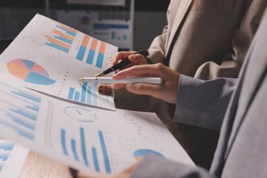 Group of confident business people point to graphs and charts to analyze market data, balance sheet, account, net profit to plan new sales strategies to increase production capacity.