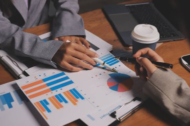 Group of confident business people point to graphs and charts to analyze market data, balance sheet, account, net profit to plan new sales strategies to increase production capacity.