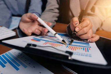 Group of confident business people point to graphs and charts to analyze market data, balance sheet, account, net profit to plan new sales strategies to increase production capacity.