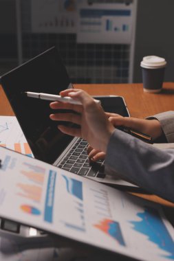 Group of confident business people point to graphs and charts to analyze market data, balance sheet, account, net profit to plan new sales strategies to increase production capacity.