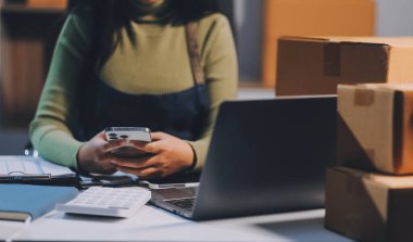 Girişim KOBİ küçük işletme girişimcisi önlük giyen Asyalı kadın dizüstü bilgisayar ve kutu kullanarak çevrimiçi müşterilere, çevrimiçi sme iş fikirlerine satış hazırlamak için siparişleri alır ve gözden geçirir.