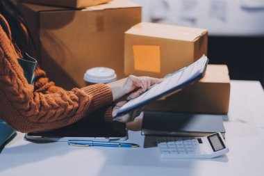 Girişim KOBİ küçük işletme girişimcisi önlük giyen Asyalı kadın dizüstü bilgisayar ve kutu kullanarak çevrimiçi müşterilere, çevrimiçi sme iş fikirlerine satış hazırlamak için siparişleri alır ve gözden geçirir.