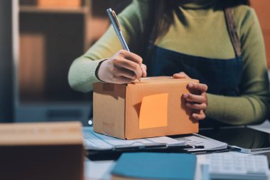 Girişim KOBİ küçük işletme girişimcisi önlük giyen Asyalı kadın dizüstü bilgisayar ve kutu kullanarak çevrimiçi müşterilere, çevrimiçi sme iş fikirlerine satış hazırlamak için siparişleri alır ve gözden geçirir.