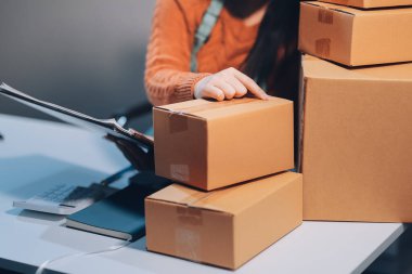 Girişim KOBİ küçük işletme girişimcisi önlük giyen Asyalı kadın dizüstü bilgisayar ve kutu kullanarak çevrimiçi müşterilere, çevrimiçi sme iş fikirlerine satış hazırlamak için siparişleri alır ve gözden geçirir.