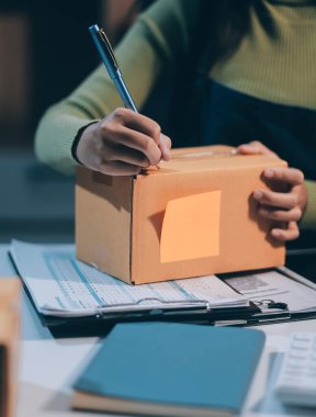 Girişim KOBİ küçük işletme girişimcisi önlük giyen Asyalı kadın dizüstü bilgisayar ve kutu kullanarak çevrimiçi müşterilere, çevrimiçi sme iş fikirlerine satış hazırlamak için siparişleri alır ve gözden geçirir.