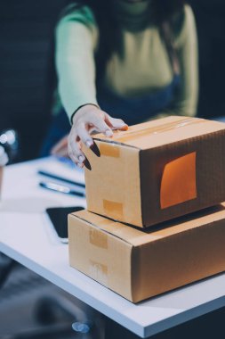 Girişim KOBİ küçük işletme girişimcisi önlük giyen Asyalı kadın dizüstü bilgisayar ve kutu kullanarak çevrimiçi müşterilere, çevrimiçi sme iş fikirlerine satış hazırlamak için siparişleri alır ve gözden geçirir.