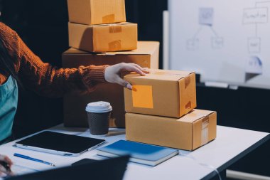 Girişim KOBİ küçük işletme girişimcisi önlük giyen Asyalı kadın dizüstü bilgisayar ve kutu kullanarak çevrimiçi müşterilere, çevrimiçi sme iş fikirlerine satış hazırlamak için siparişleri alır ve gözden geçirir.