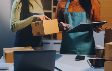 Girişim KOBİ küçük işletme girişimcisi önlük giyen Asyalı kadın dizüstü bilgisayar ve kutu kullanarak çevrimiçi müşterilere, çevrimiçi sme iş fikirlerine satış hazırlamak için siparişleri alır ve gözden geçirir.