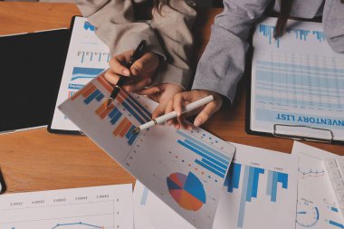 Group of confident business people point to graphs and charts to analyze market data, balance sheet, account, net profit to plan new sales strategies to increase production capacity.