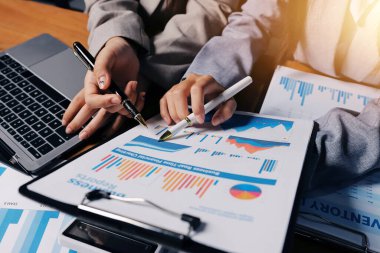 Group of confident business people point to graphs and charts to analyze market data, balance sheet, account, net profit to plan new sales strategies to increase production capacity.