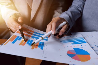 Group of confident business people point to graphs and charts to analyze market data, balance sheet, account, net profit to plan new sales strategies to increase production capacity.