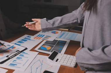 Group of confident business people point to graphs and charts to analyze market data, balance sheet, account, net profit to plan new sales strategies to increase production capacity.