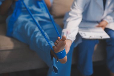 Kendine güvenen fizyoterapist, hastanın bacağını klinik odasında gerdirerek direnç bandı kullanmasına yardım ediyor..