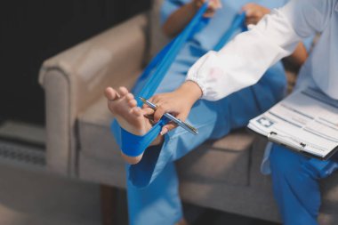 Kendine güvenen fizyoterapist, hastanın bacağını klinik odasında gerdirerek direnç bandı kullanmasına yardım ediyor..