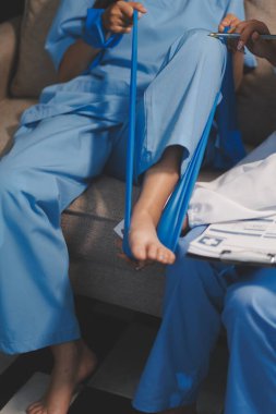 Kendine güvenen fizyoterapist, hastanın bacağını klinik odasında gerdirerek direnç bandı kullanmasına yardım ediyor..