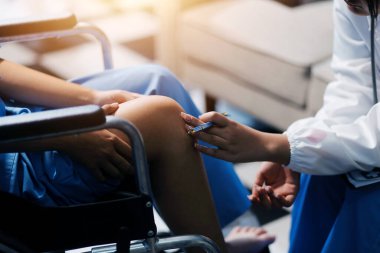 Kadın bir doktor, eklem iltihabı nedeniyle diz ağrısı olan yaşlı bir hastayı muayene eder. Hastaya iyileşme sürecinde yardım ediliyor, ağrı yönetimi ve hareket kabiliyetinin iyileştirilmesi üzerinde duruluyor..