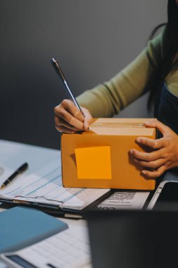 Girişim KOBİ küçük işletme girişimcisi önlük giyen Asyalı kadın dizüstü bilgisayar ve kutu kullanarak çevrimiçi müşterilere, çevrimiçi sme iş fikirlerine satış hazırlamak için siparişleri alır ve gözden geçirir.