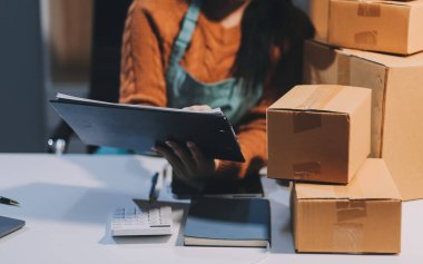 Girişim KOBİ küçük işletme girişimcisi önlük giyen Asyalı kadın dizüstü bilgisayar ve kutu kullanarak çevrimiçi müşterilere, çevrimiçi sme iş fikirlerine satış hazırlamak için siparişleri alır ve gözden geçirir.